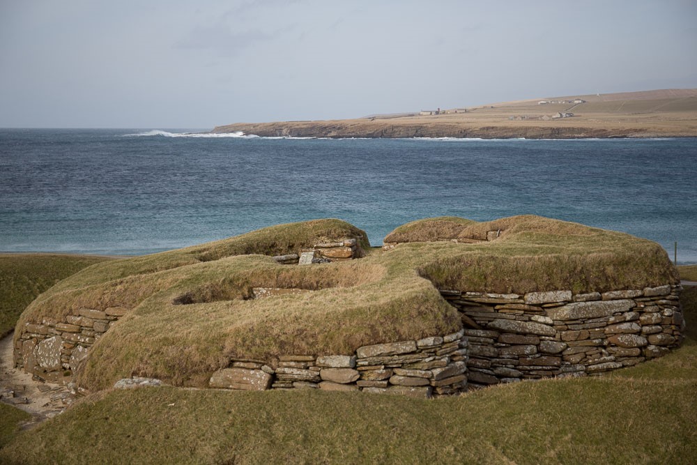Rounded walls of piled-up flat stones, with turf growing on top. The sea in the background.