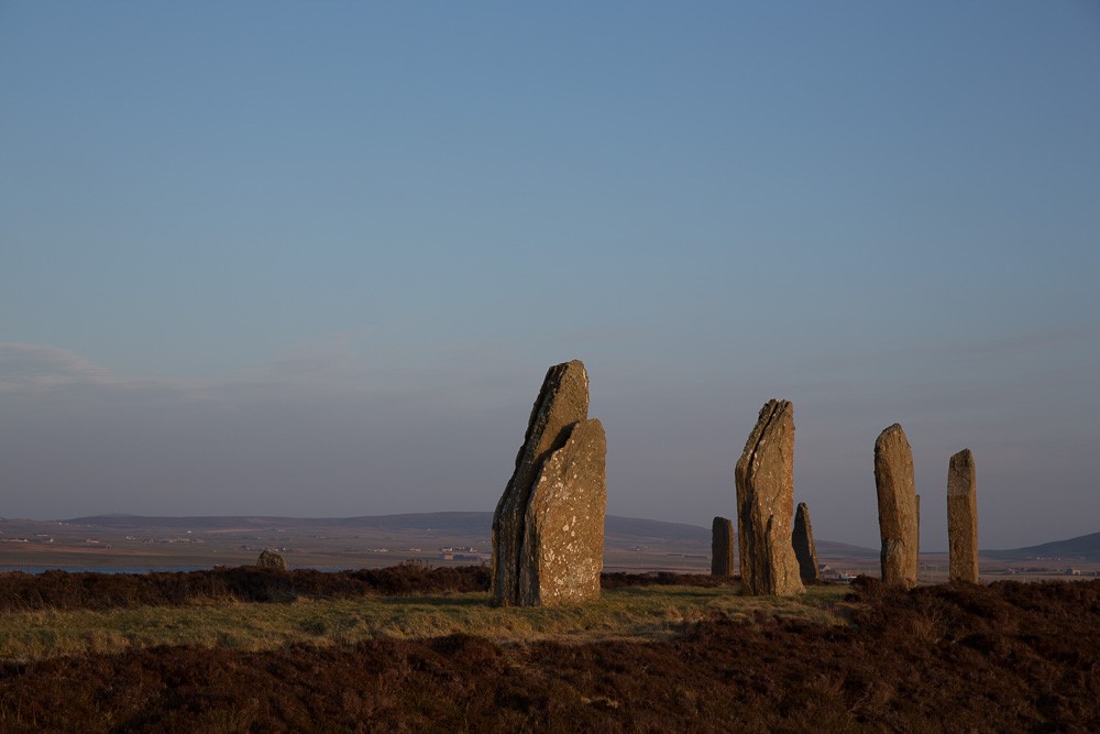 Large standing stones in a row on a flat field, low hills in the background.