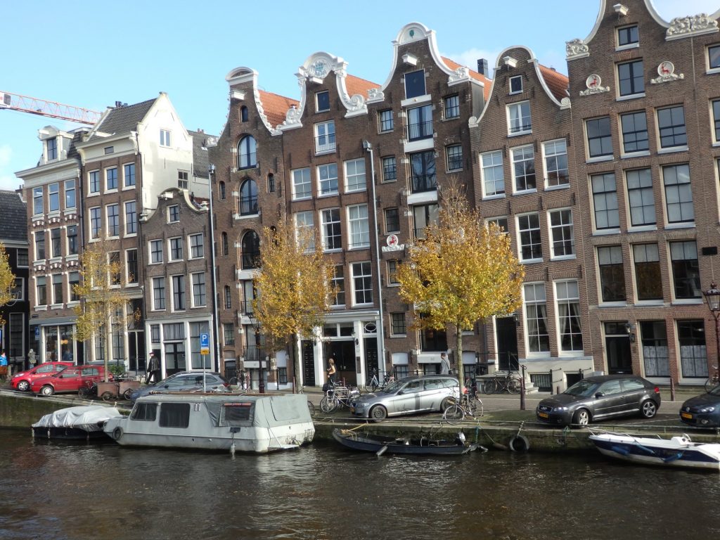 A row of brick rowhouses and former warehouses along a canal: each is quite narrow with a decorative gable and many large windows.