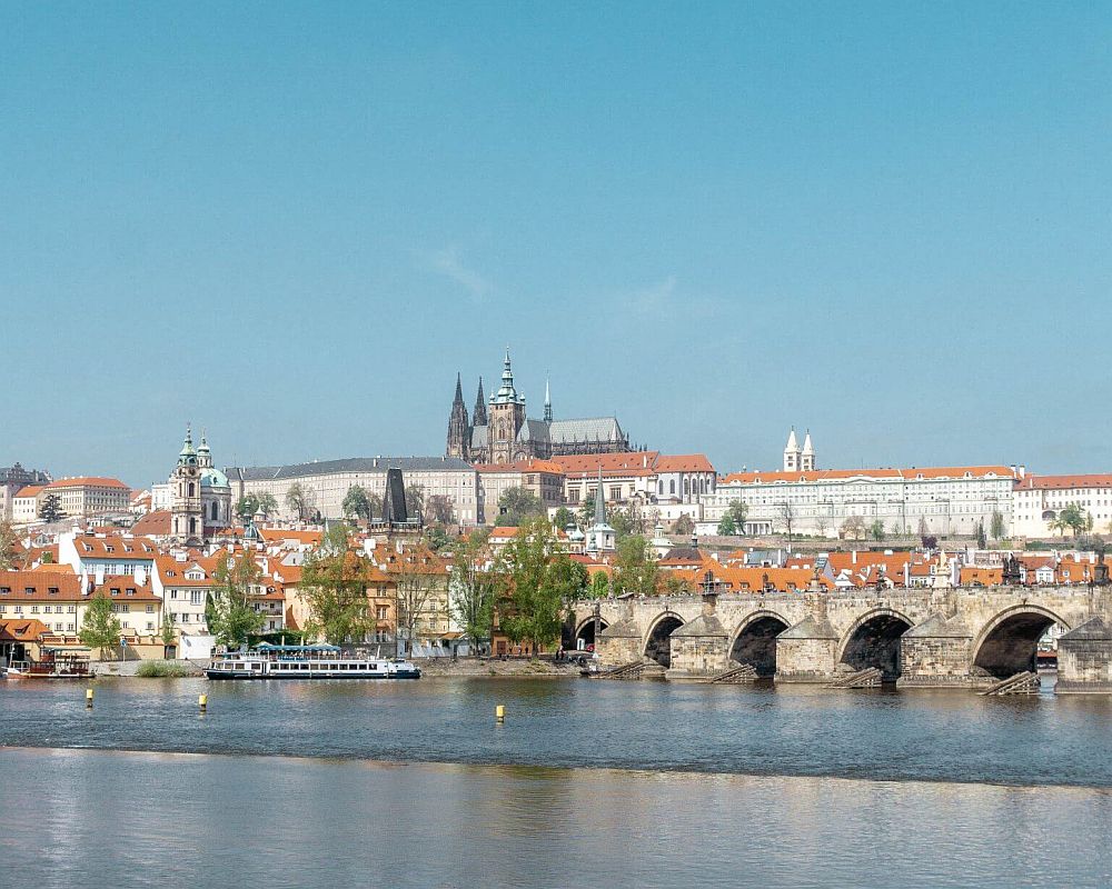 A view across the river  with the Charles Bridge and behind it, a cluster of red-tile roofed buildings with the spires of Prague Castle above them.