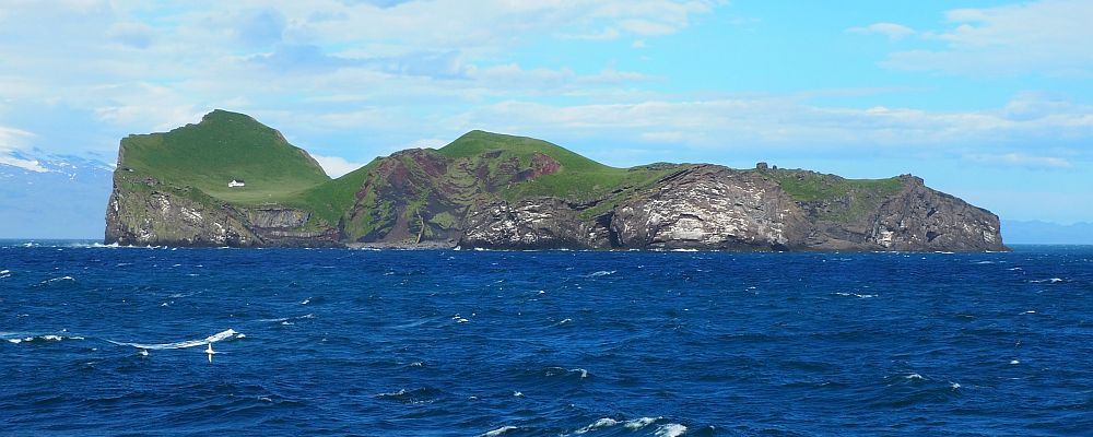 An island surrounded by blue sea. The island has steep granite cliffs all around, and green land on the top.