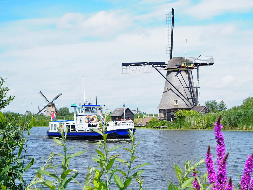 Looking across a canal, a boat passing in front of two windmills on the opposite bank.