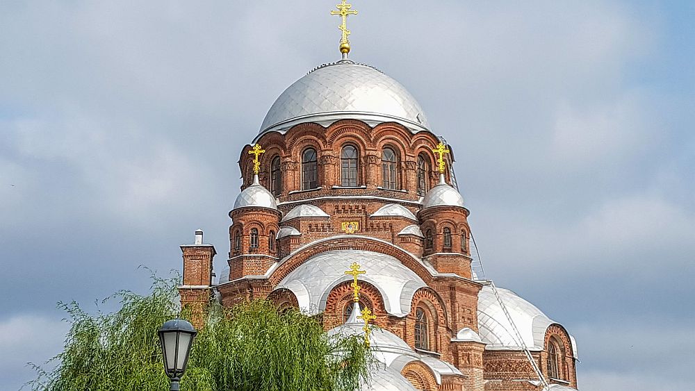 The domes of a basilica: red brick building with arched windows and a big silver dome in the middle, with smaller ones around it.