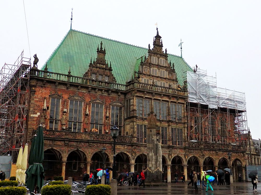 The building has an arched portico along the ground floor, decorative statues and other decoration between the windows on the upper floor, three decorative gables in front of the steep green roof, the middle gable the largest.