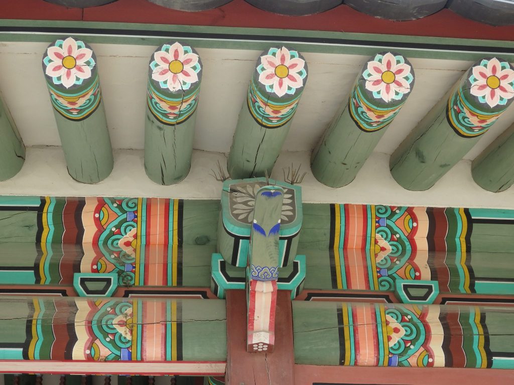 A detail of the paintwork on one of the Changdeokgung palace buildings: detailed decorative flourishes, including colorful 6-petaled flowers on the end of each round beam.