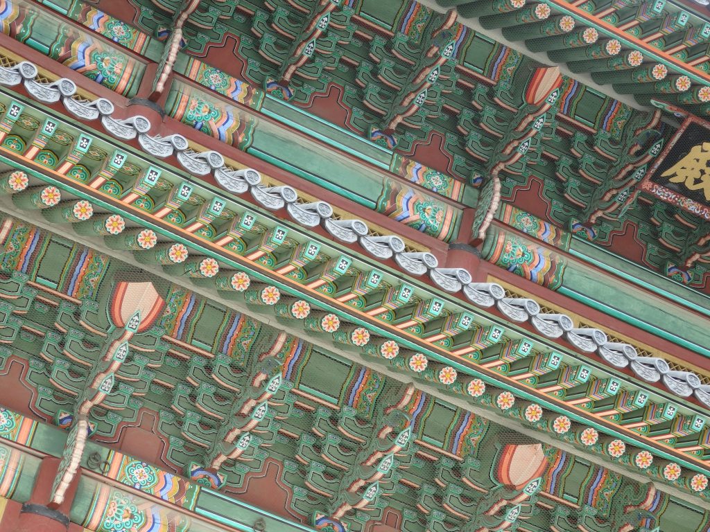 A larger shot of the eaves of a Changdeokgung Palace building: the dominant color is green, but the ends and edges of every piece of the structure are decorated with colorful patterns.
