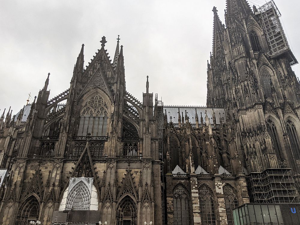 Side view of the cathedral, with the spires at the right and a side entrance in front. Incredibly ornate in typical gothic style, with gothic arched windows, flying buttresses and elaborate sculptural details around every available surface.