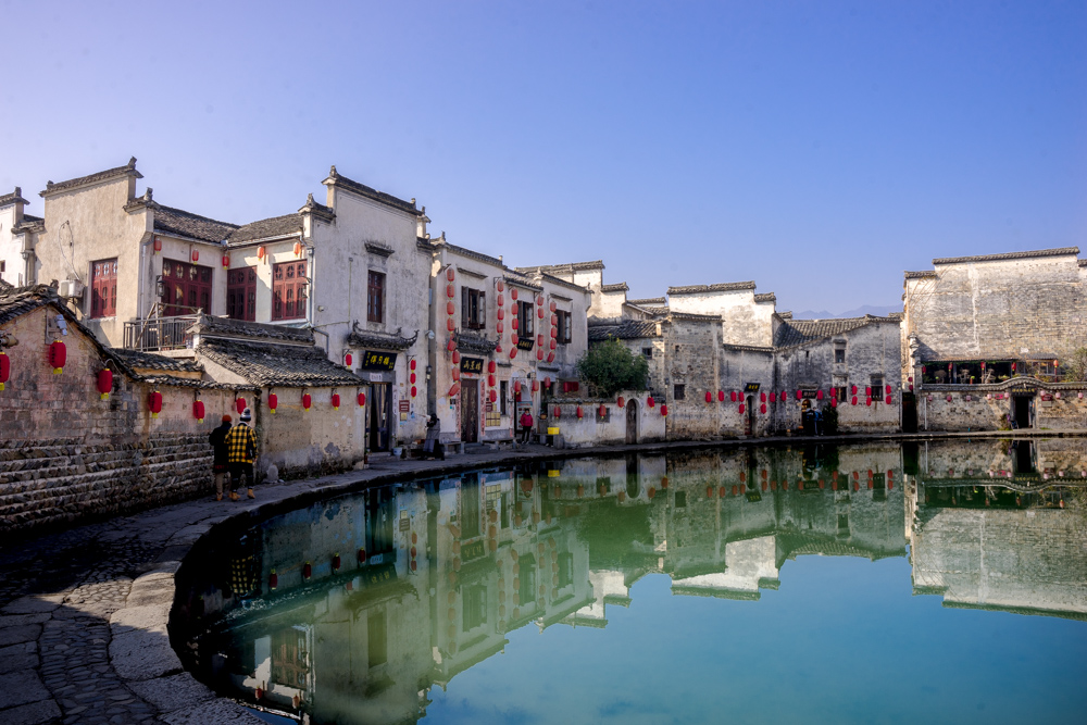 A row of white houses around the curved edge of a lake. The houses are simple and flat-fronted mostly, 2 storeys tall, and decorated with bright red paper lanterns.