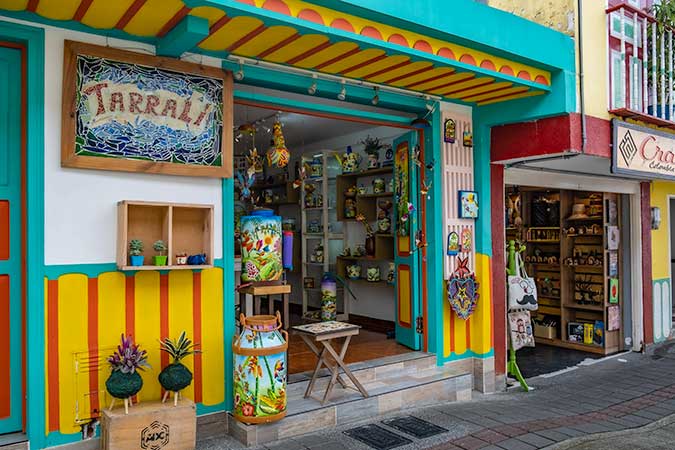 A colorful storefront: a large opening to the street, trip painted in aqua blue, red and yellow. A mosaic sign reads Tarrali.