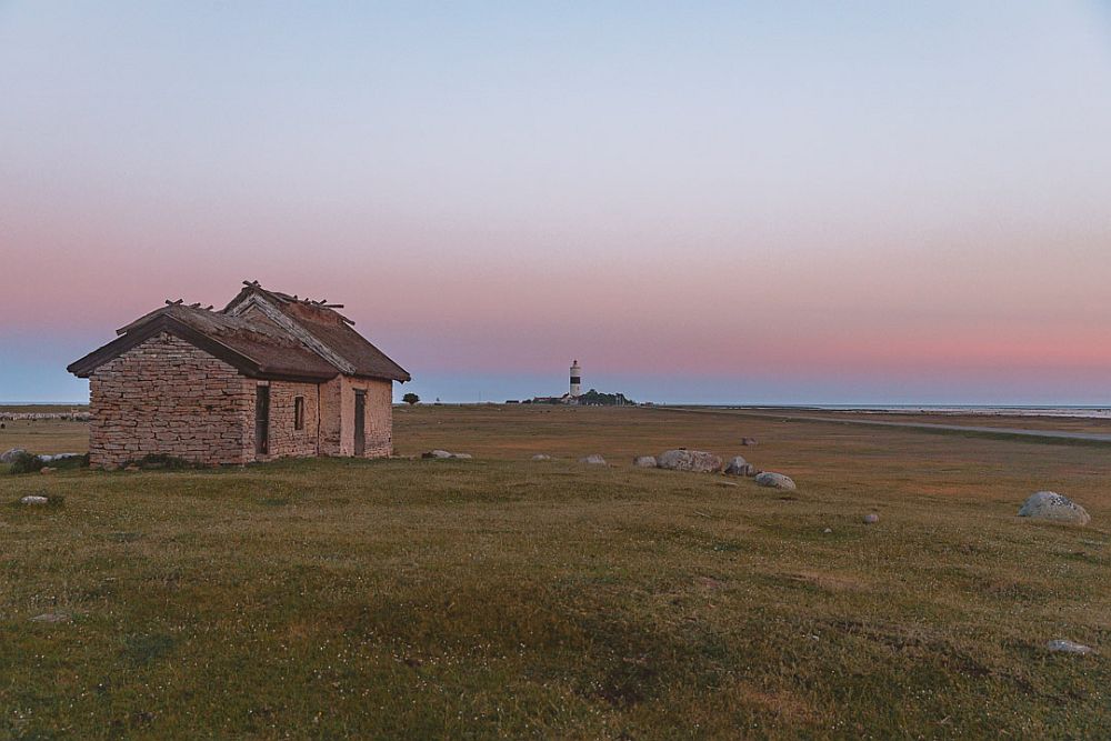 A solitary small house in a hill covered in short grasses, against a sunset sky.