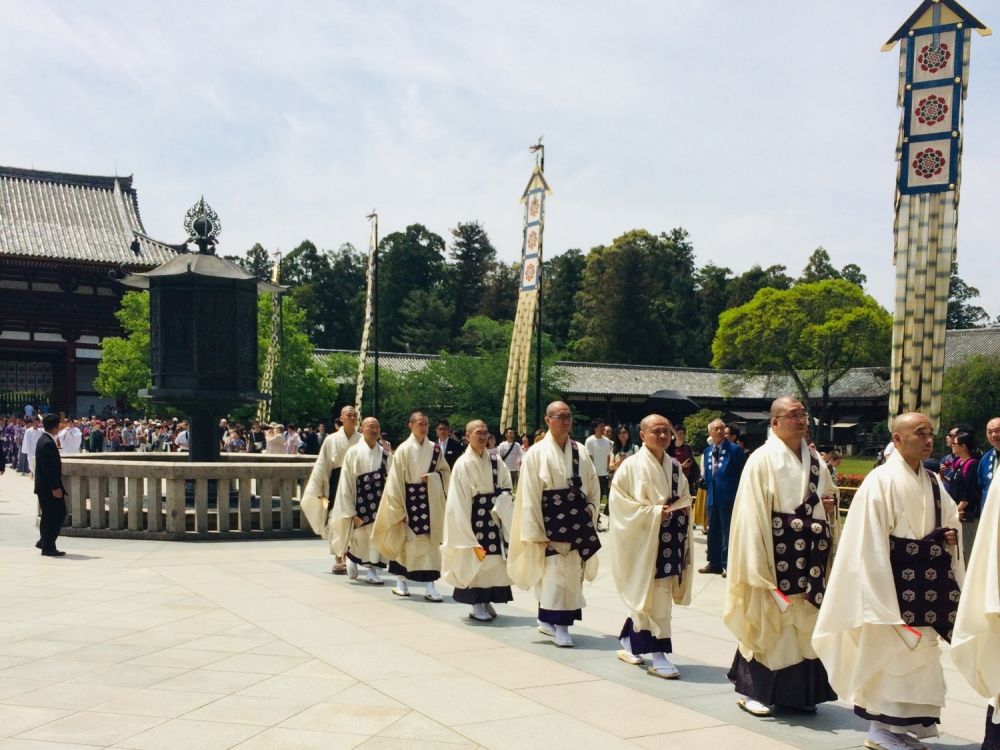 A procession of monks wearing white robes with some sort of wide dark belt around their middles.