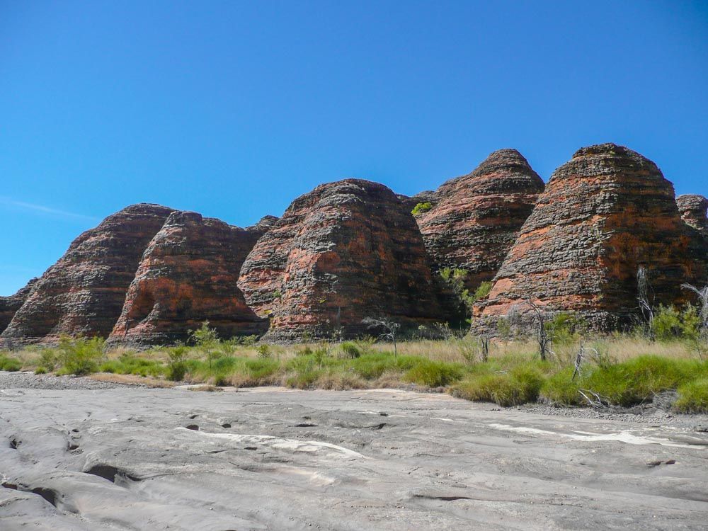 A closer view of the rock formations in Purnululu: cone-shaped, but rounded, reddish stone with darker horizontal stripes.