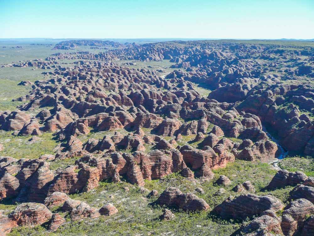 The Bungle Bungles as seen from above: a collection of conical rock formations in reddish stone standing on a flat grassy plain.