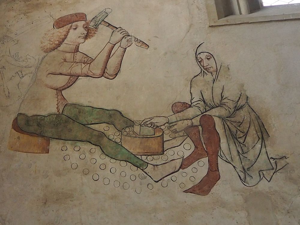 A fresco of two people in medieval style tunics with tights. Left, a person sits and raises a hammer. Right, a person sits facing the first person and places something on a block between them.