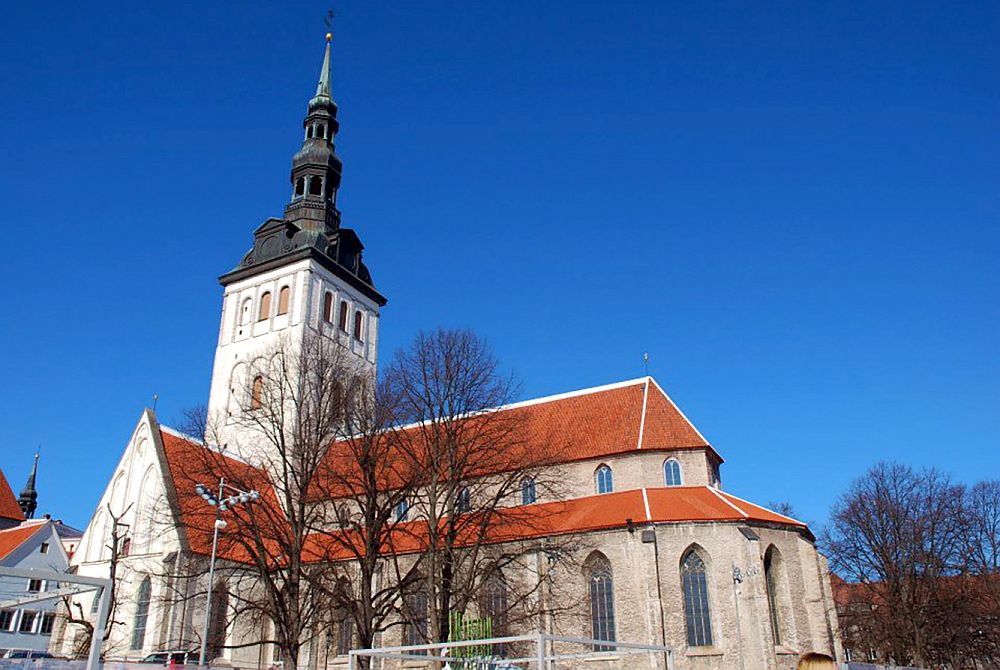 A church, seen from the side and behind. The right-hand end (the back of the church) is round and brick, with Gothic arched windows in a line around the curve. To the left, the front of the church is painted white, and has a big square spire, also white except for its dark roof.