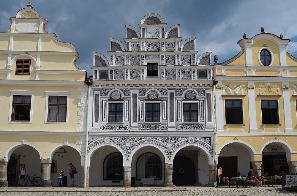 Three of the row of houses, only the middle one complete in this photo. The ones on either side are pastel yellow with white trim. The center one is gray with very detailed and ornate white decoration and an unusual shaped stepped gable.