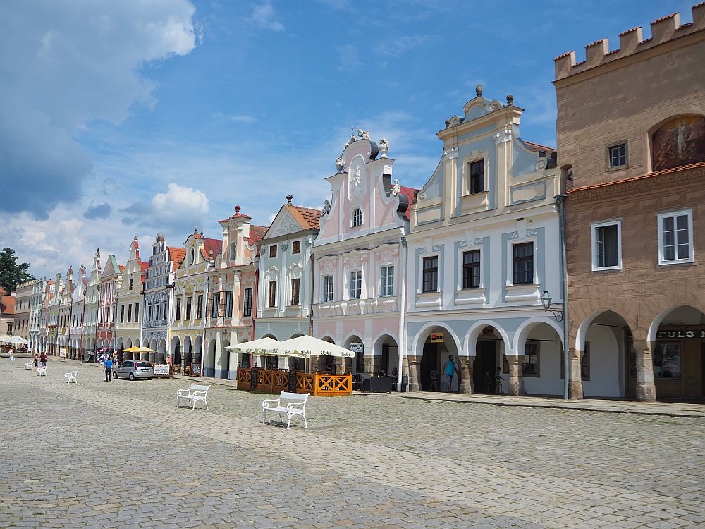 Looking across the plaza down the row of houses: an arcade held up by columns and arches along the ground floor, pretty facades of two floors above that. Each is a different pastel color.