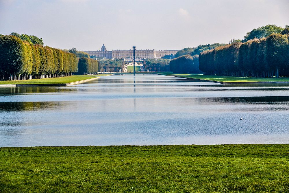 In the foreground, water (the canal). Straight ahead, far in the distance, Versailles Palace is visible: a massive structure, only perhaps 6 stories tall, but very wide - it's width is not visible in this photo because the trees on the sides of the water obscure it.