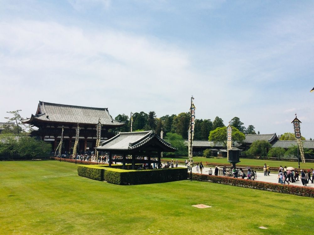 A temple in the background with curved roof, a small shelter with a similar roof nearer by, and a wide path leading out of the larger one and passing by the smaller one. In the foreground, closely cropped lawn.