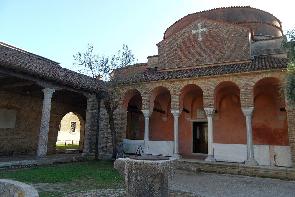 A simple brick church. Across the front an arcade with arches held up by pillars. A dome above that looks to be a bit flat on the top.