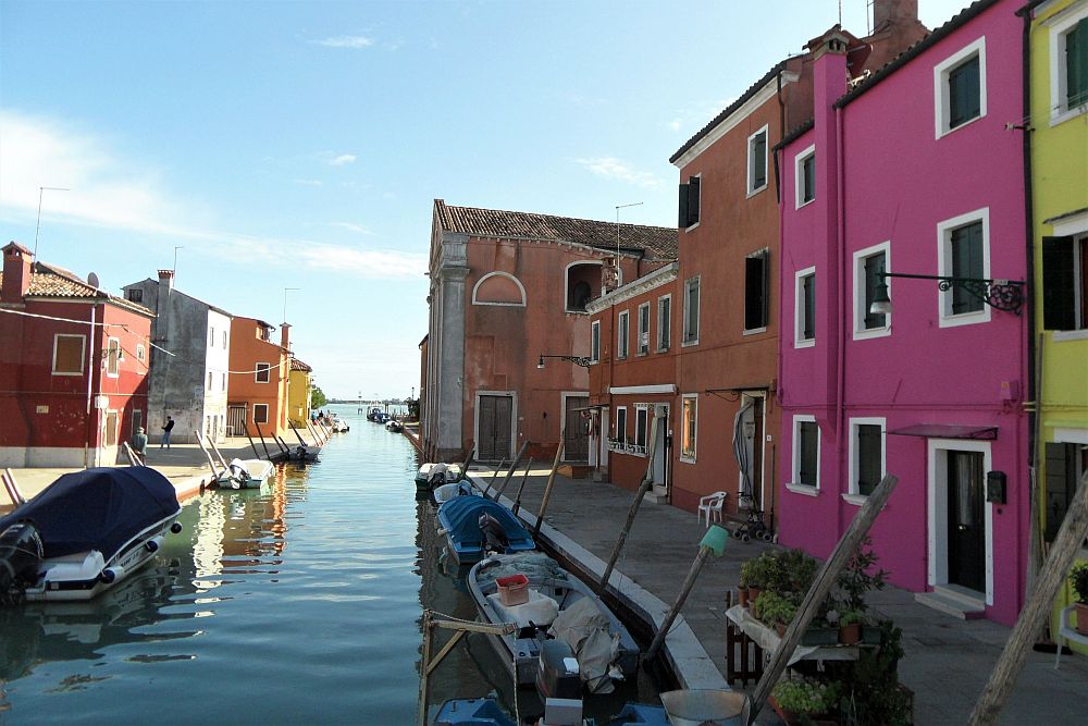 Looking down a canal with boats parked along its sides, the houses are about 3 stories tall and quite flat-fronted and simple, except that each is painted in a bright color: pink, yellow, orange for example. 