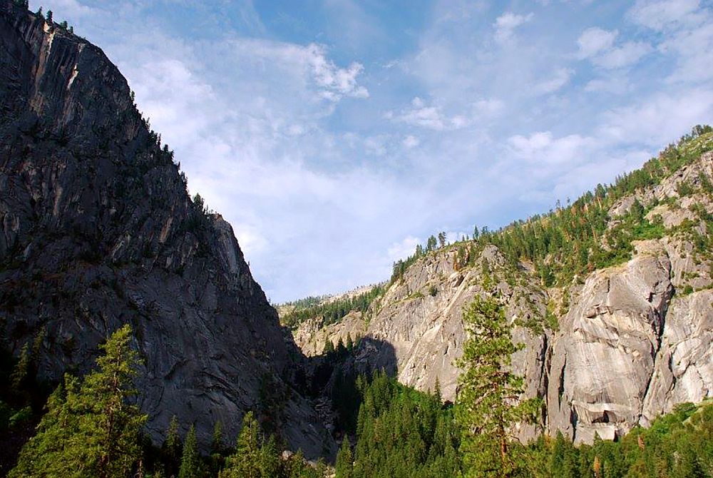 A view along a valley in Yosemite, trees in the valley, sheer rock face on the opposite side.