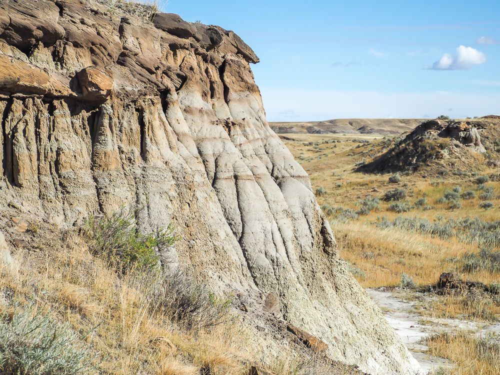 A hoodoo on the left, and beyond it, a long view into the distance with dry grasslands and hills.