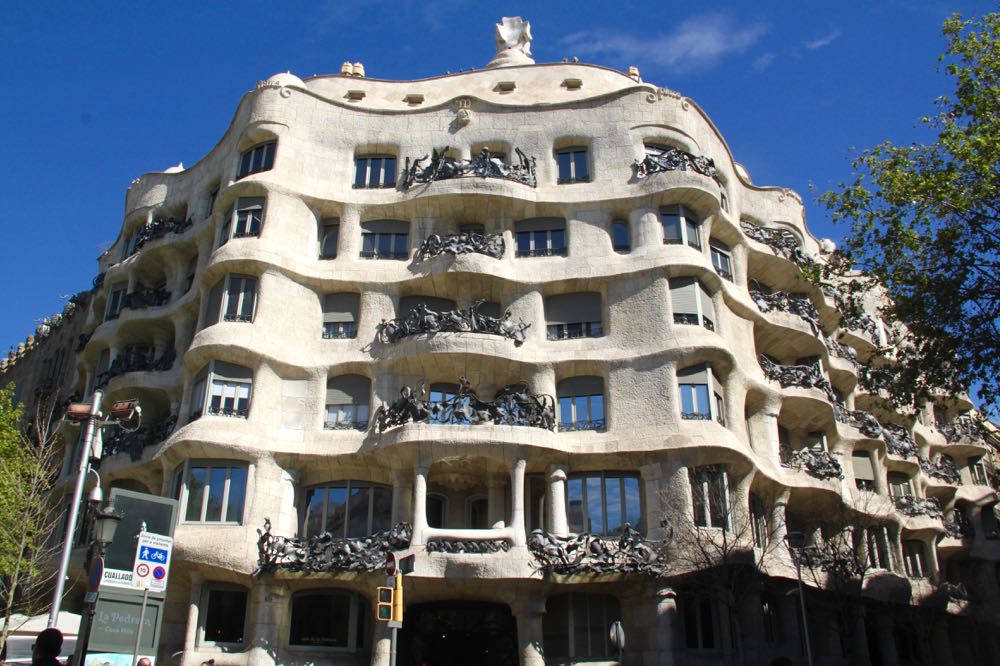 The building is white, with rounded edges as it extends around the corner of two streets. The central entrance faciing the corner isn't really visible in this shot, but the balconies above it on each of the upper 4 stories are very orante metal forms.