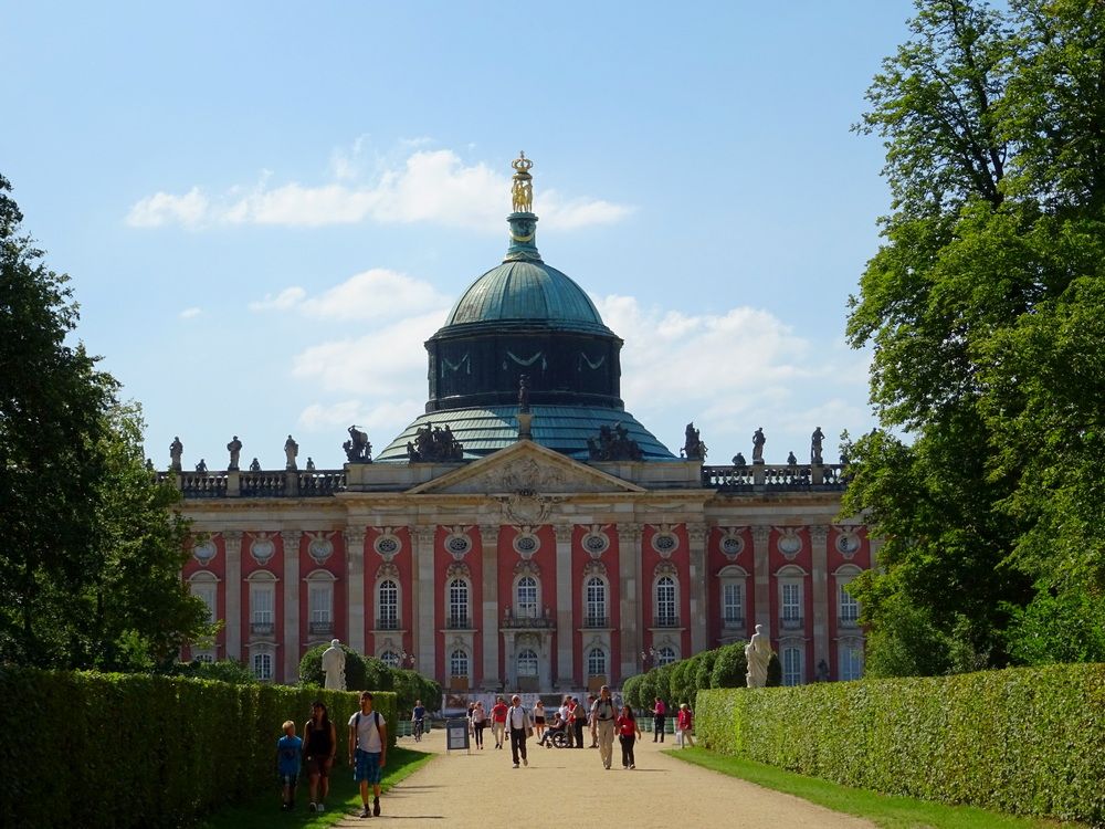 Looking down a wide path to a large palace: several stories high, it extends past the edges of the photo on both sides. Above the center is a large copper dome.