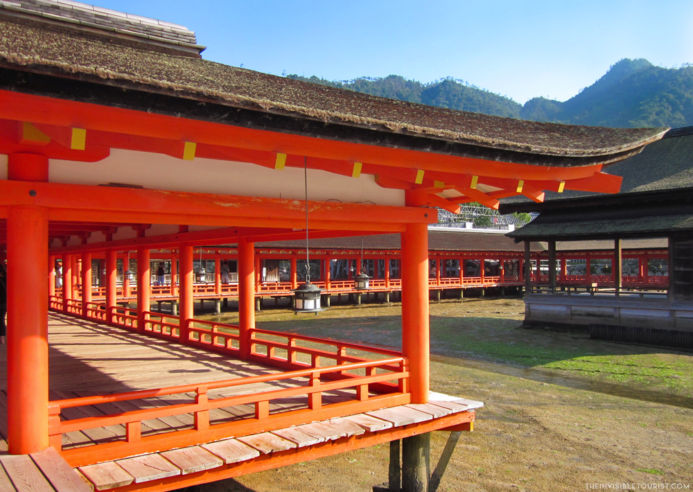 A low wooden building, painted reddish-orange with brown curved roofs. It has a long veranda along its length, open to the air.