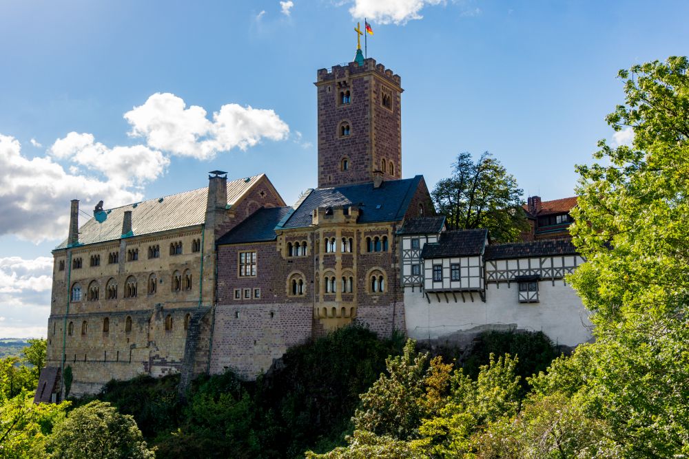 The castle is perched on a hill, with a single square tower in its middle. The left'hand wing is brick and/or stone, while the right-hand wing is white plaster with exposed timber beams.
