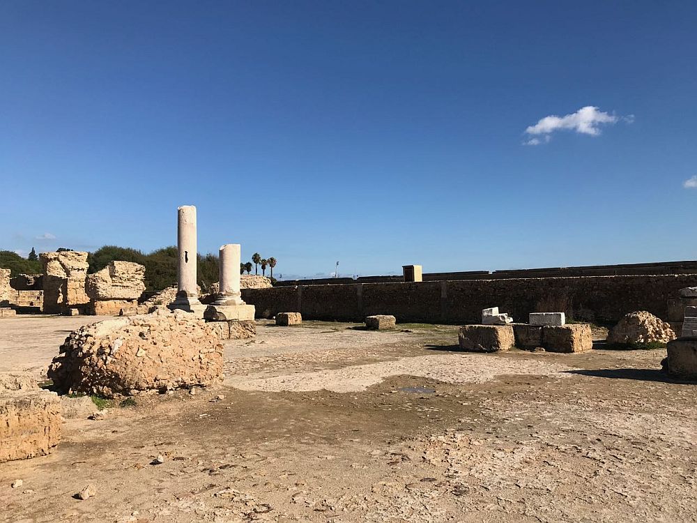 A expanse of dirt ground, with a couple of broken columns standing at the back, as well as other bits of buildings. The back of the area has a long wall bordering it.