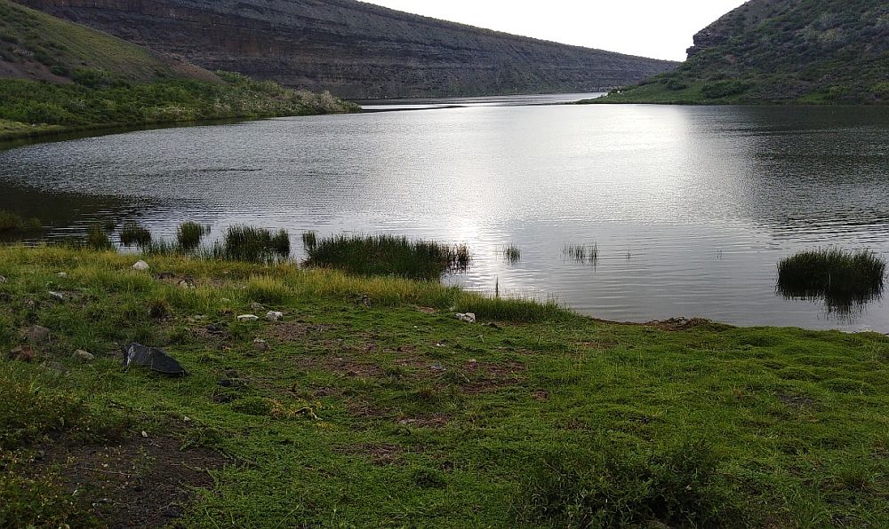 View over a lake, with light shining on the water, gentle hills around it.