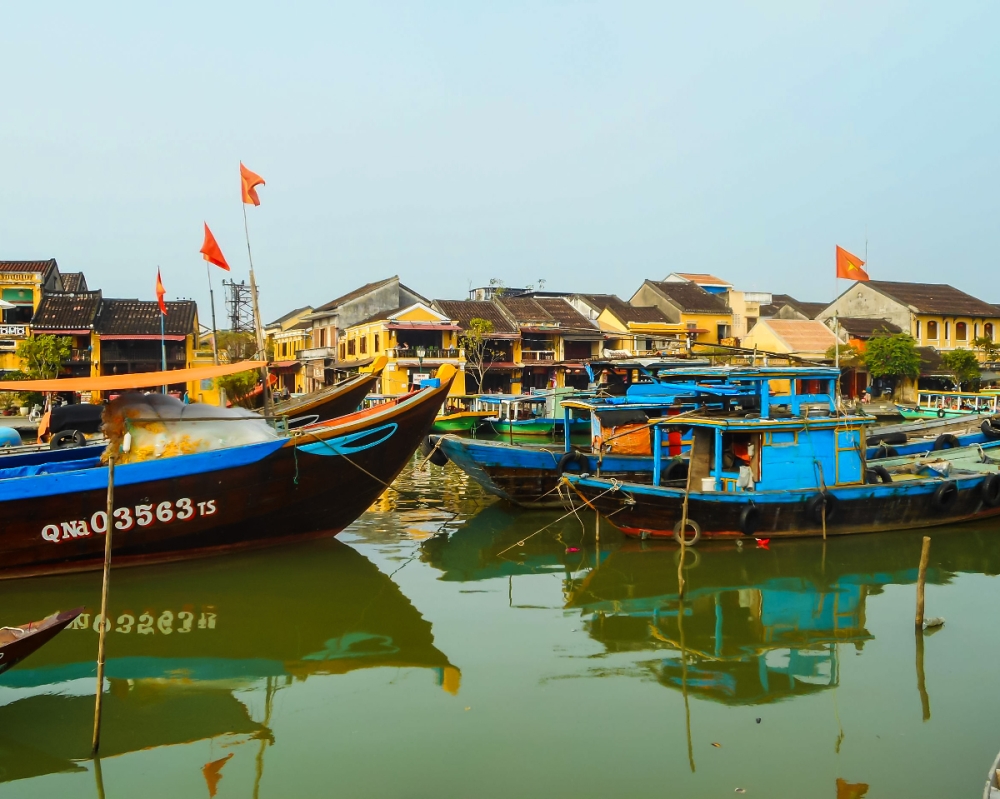 A view of the harbor, with traditional boats (sampans) moored next to each other, painted in shades of blue. Beyond them are the houses on the waterfront, though they are hard to see with the boats blocking them.