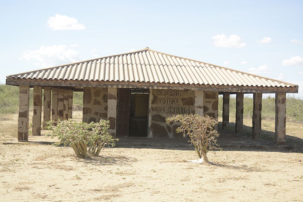 A low single-story stone building, with the metal roof extending over a covered space on all three visible sides. A sign on the building reads Koobi Fora Museum.