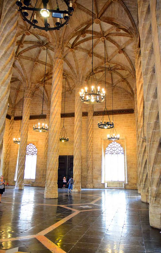 A view of a part of the inside of La Lonja. The ceiling has gothic arches, held up by tall slender columns that are caved in a spiral pattern. Judging by the people who look very small at the bottom of the photo, the ceiling is perhaps five or six stories high.