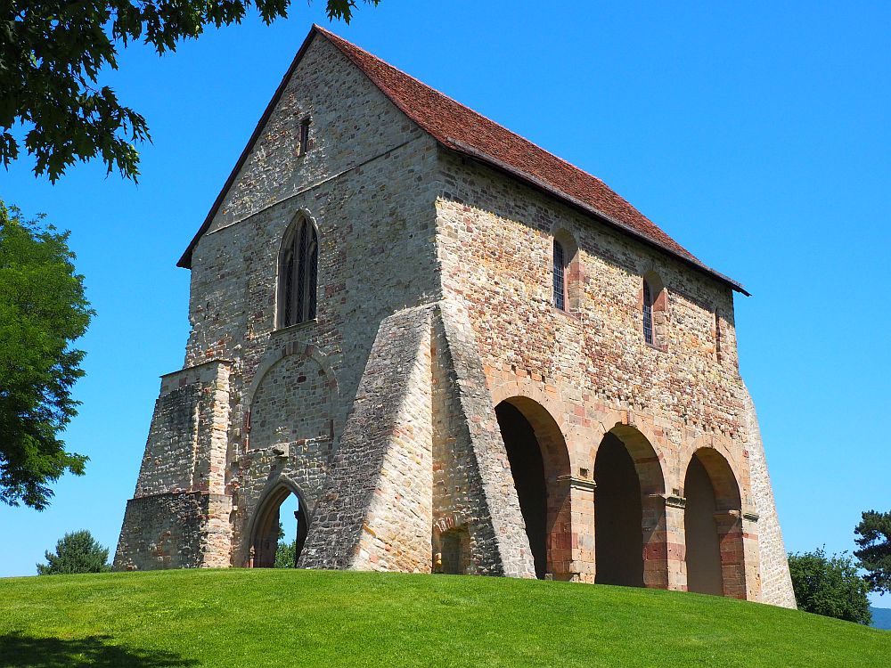 The church at Lorsch is a simple rectangle, a remnant of something much larger. It is made of brick and has a small archway above the entrance at the front. The sides have much larger archways: the one that shows in this photo has 3 archways along the side. The upper story has smaller arched windows. The corners have heavy buttresses.