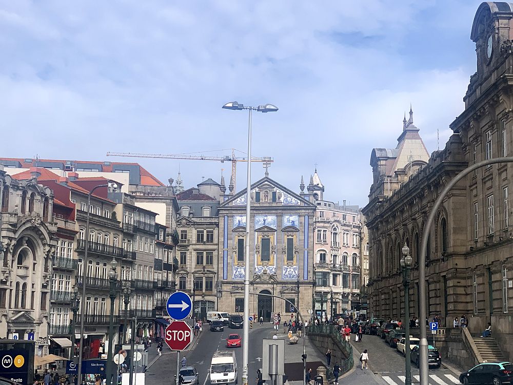 Sighting down a wide city street with apartment buildings on the left, about 5 stories tall with french balconies on each floor. On the right, a large official-looking building in some neo-classical style, in stone. Straight ahead, at the end of the road, the theater, I think, with blue-tiled images above and below the windows in the center of the facade and also up inside the pediment at the top.