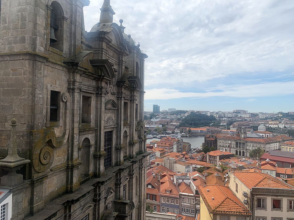 On the left, the façade of a large building, perhaps a church, made of stone with a flat façade but decorative windows. Straight ahead, a view over the red roofs of the city.