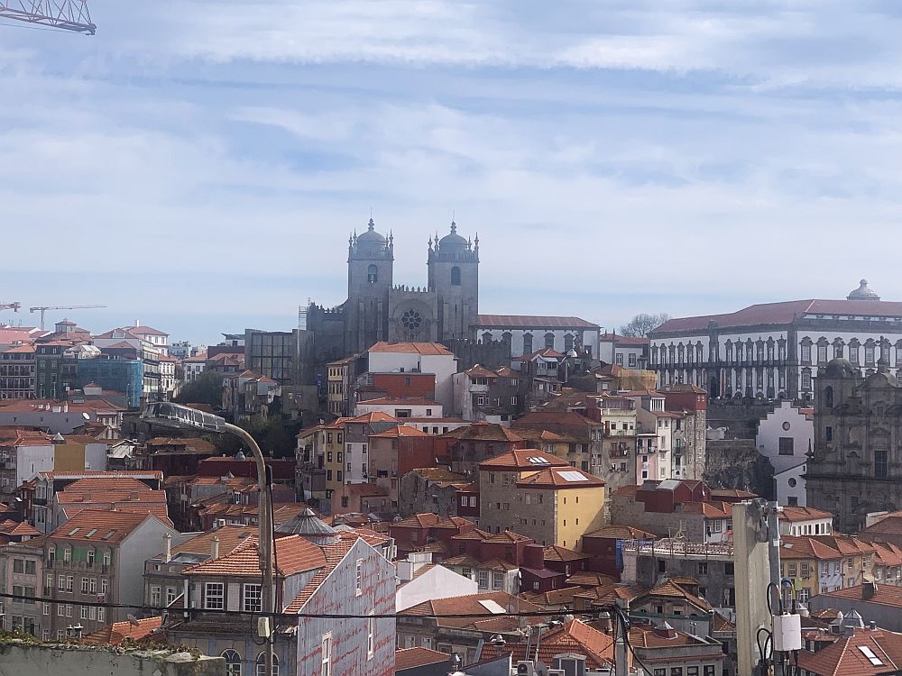 A view over the city, mostly low-rise with red tile roofs. In the background, the cathedral, with two short and stocky towers. 