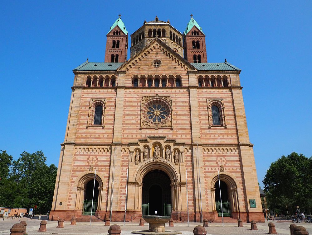 The Cathedral's front: three arched entrances on the ground floor, a rose window flanked by two arched windows above that, and a row of small pillars above that. A bit of the 8-sided cupola is visible along with two slender square towers on either side of the cupola. The walls are relatively unadorned, just stripes of red and light brown bricks, except for the row of carved images of saints above the central archway.