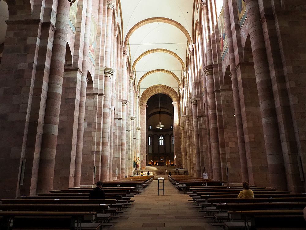 A long narrow central space, with tall pillars on each side. The roof is held up by simple rounded arches across the space. Many rows of pews facing the altar at the end, which is darker than the main space so it isn't visible in this photo.