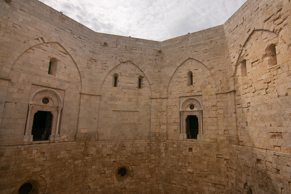 Inside the octagonal courtyard: 4 sides are visible, each with a shallow gothic arch and two of them with a romanesque archway and doorway inside the gothic arch.