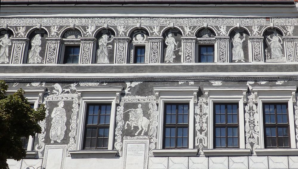 White trim around the windows of the two stories that are visible in this photo. Between the windows, ornate patterns and human figures in togas in white on a dark gray background.