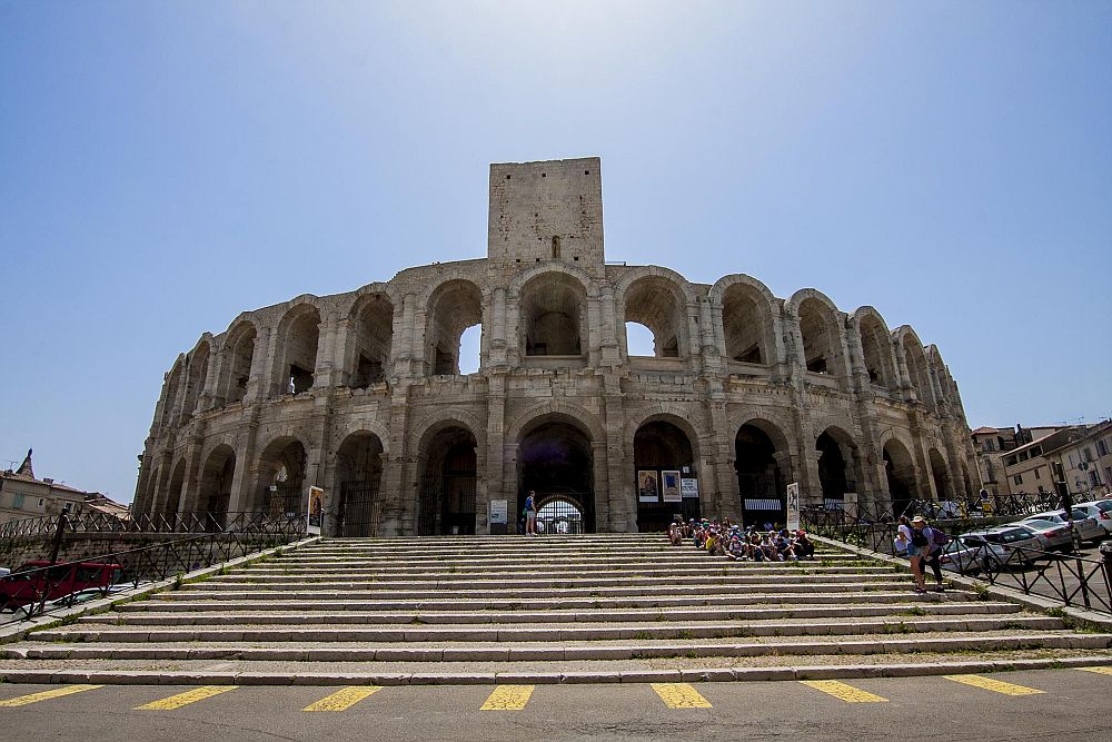 Looking up a long flight of stairs at a Roman amphitheater: rounded arches all around the curves structure on both storeys.