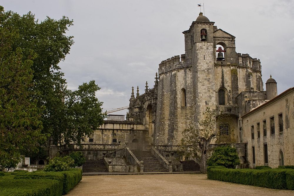 External view of the Convent of Christ in Tomar, Portugal: a stone building whose main section is round and several stories high, toped with a cluster of small bell towers.