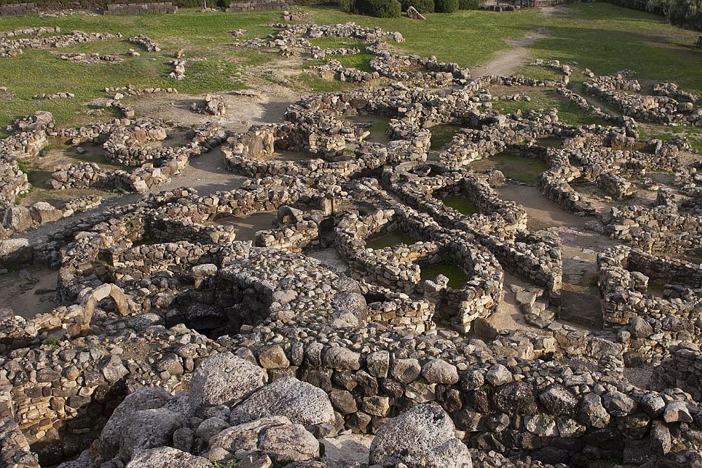 Looking down from slightly above at Su Nuraxi di Barumini onto the ruins of round stone houses. The bases of their walls still stand.