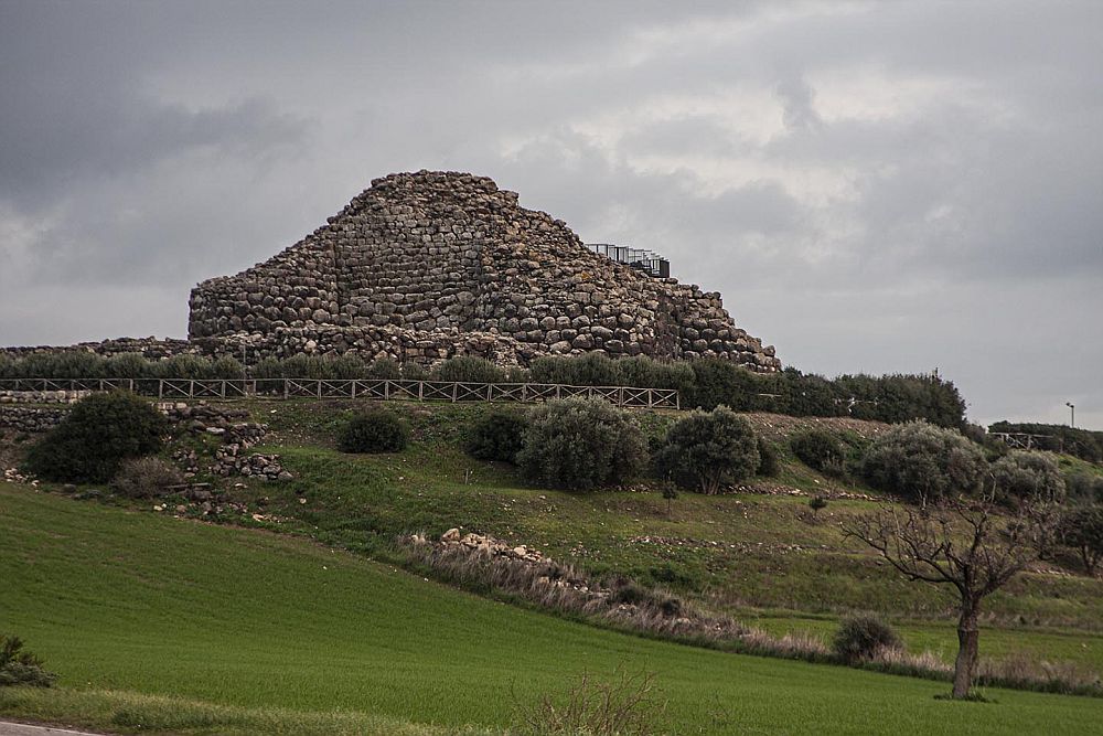 At Su Nuraxi di Barumini a structure made of rocks forms a low cone shape on a hill. 