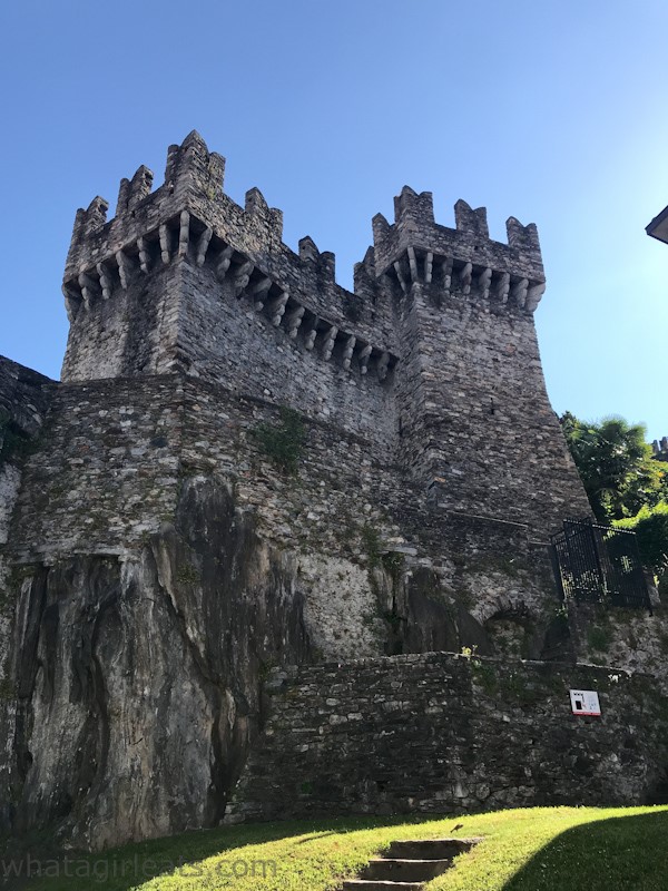 As seen from the ground, looking up at the walls: stone walls with a tower above the walls. The tower has crenellations around the top.