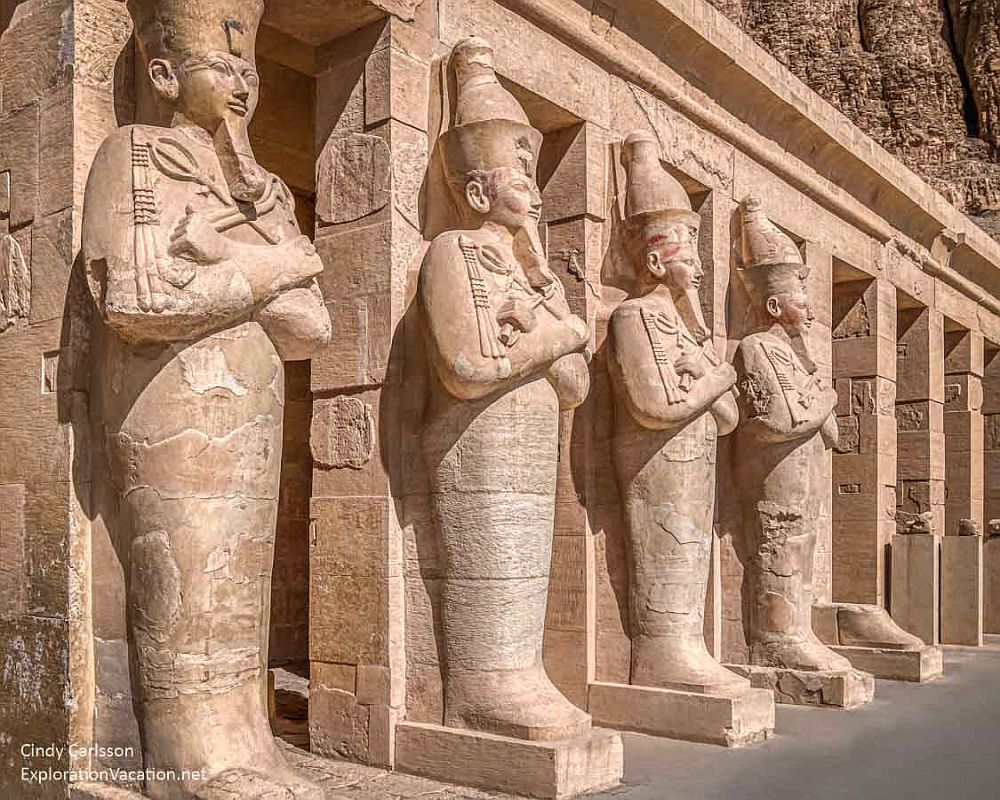 A row of four enormous statues, seen from the side, guard the entranceways to the temple. Each has its arms crossed across its chest and each has a long straight beard.